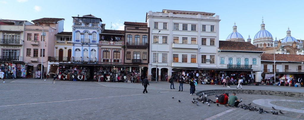 Grosser Platz mit Geschäften aum Aussenrand, Tauben und Menschen laufen über den Platz