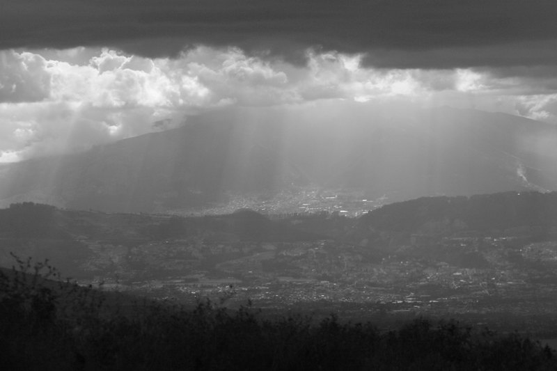 Wolken hängen tief Sonnenstrahlen kommen durch die Wolken im Hintergrund eine Stad vor einem riesigen Berg