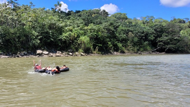drei Personen treiben in Luftreifen einen Fluss hinab